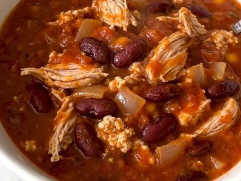A top-down view of a black slow cooker filled with a rich, hearty turkey and bean cheeseburger chili.