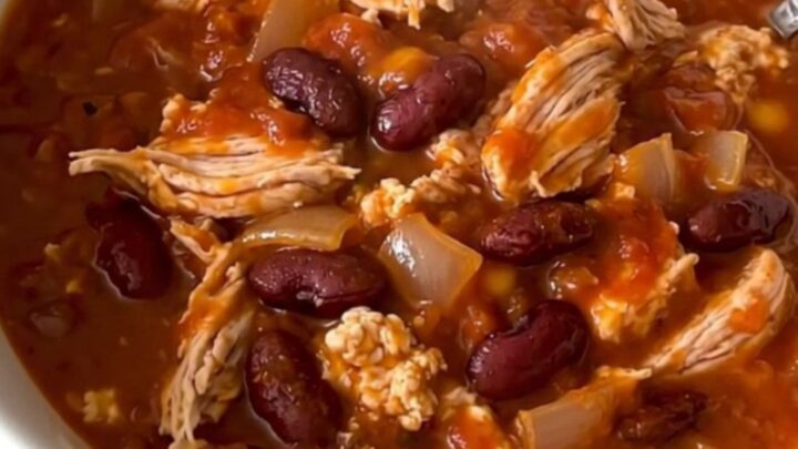 A top-down view of a black slow cooker filled with a rich, hearty turkey and bean cheeseburger chili.