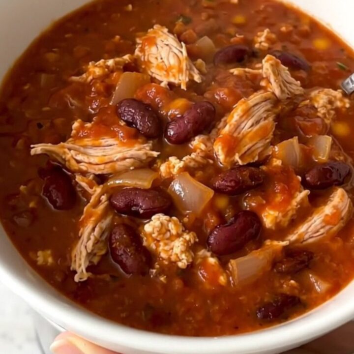 A top-down view of a black slow cooker filled with a rich, hearty turkey and bean cheeseburger chili.