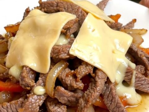 A close-up of a slow cooker filled with tender strips of round steak, sliced peppers