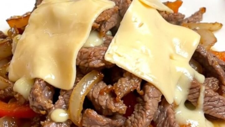 A close-up of a slow cooker filled with tender strips of round steak, sliced peppers