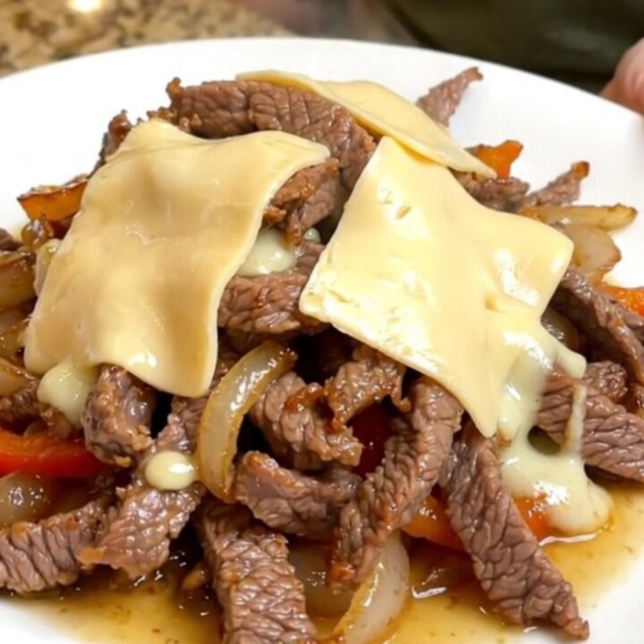 A close-up of a slow cooker filled with tender strips of round steak, sliced peppers