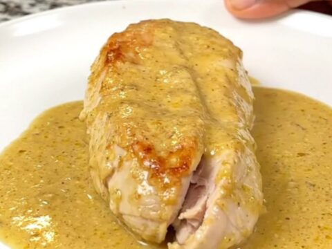 A close-up of whole cooked chicken breasts smothered in a thick, creamy honey Dijon sauce in a black slow cooker.