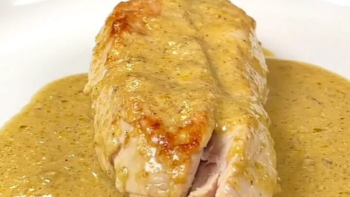 A close-up of whole cooked chicken breasts smothered in a thick, creamy honey Dijon sauce in a black slow cooker.