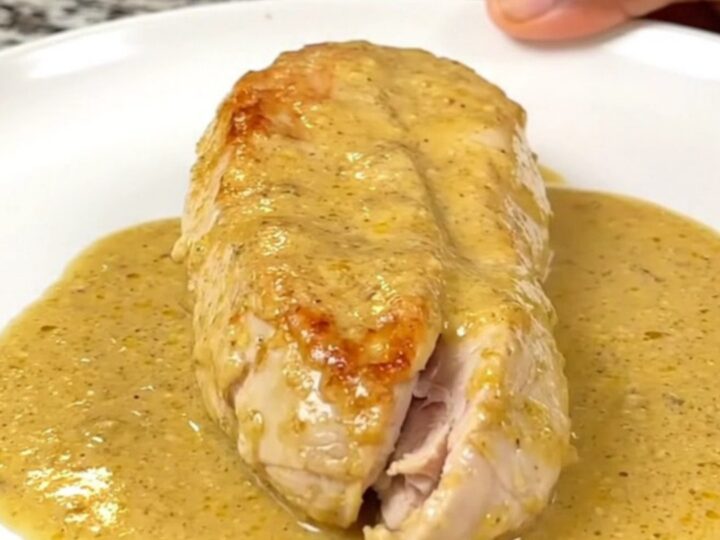 A close-up of whole cooked chicken breasts smothered in a thick, creamy honey Dijon sauce in a black slow cooker.