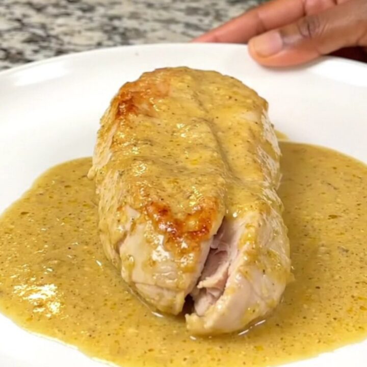 A close-up of whole cooked chicken breasts smothered in a thick, creamy honey Dijon sauce in a black slow cooker.