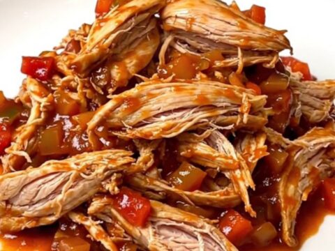 A close-up of a bowl filled with tender, shredded chicken in a rich, red sloppy joe sauce.