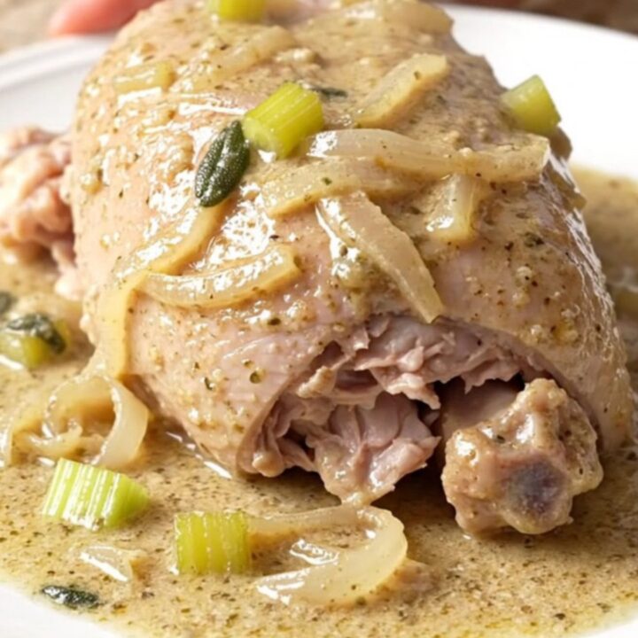A close-up of tender, braised turkey tenderloins in a creamy, herb-flecked sauce.