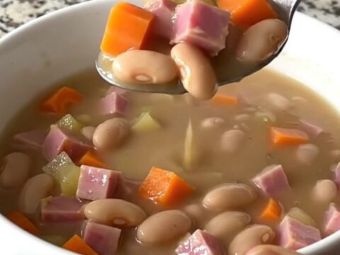 A top-down view of a black slow cooker filled with ham, beans, carrots, and onions, ready to be cooked.