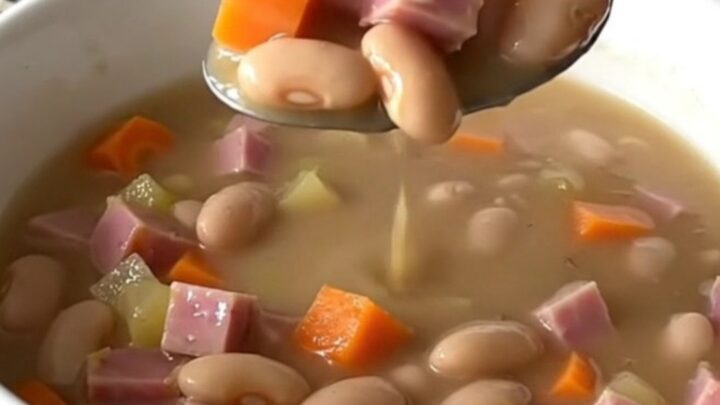 A top-down view of a black slow cooker filled with ham, beans, carrots, and onions, ready to be cooked.