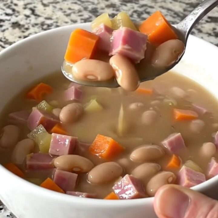 A top-down view of a black slow cooker filled with ham, beans, carrots, and onions, ready to be cooked.