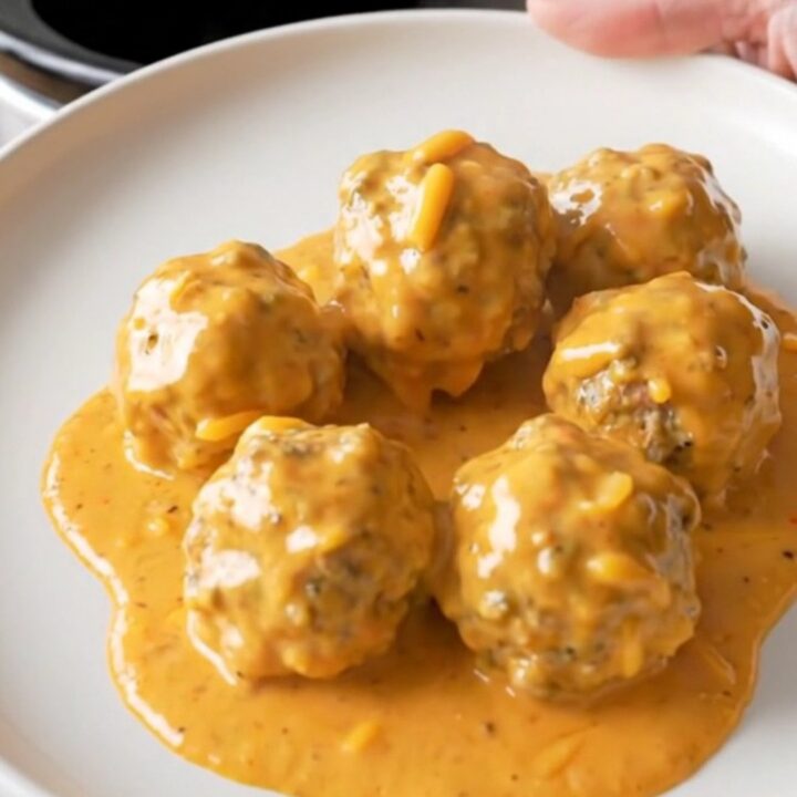 A stainless steel slow cooker filled with creamy meatballs in a rich, orange-tinted cheese sauce.