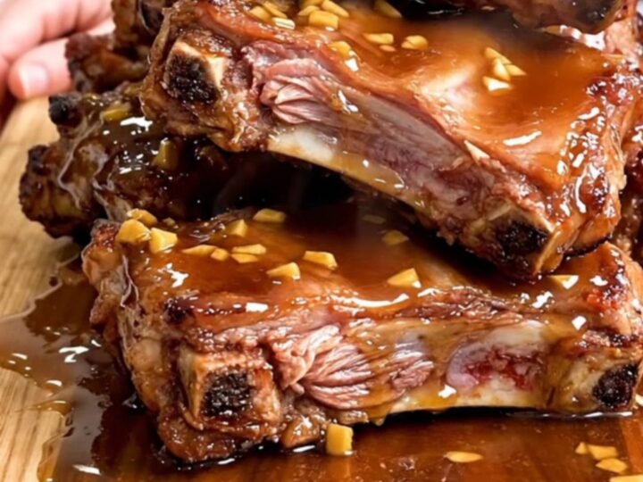 A close-up of tender, braised pork spareribs coated in a dark, glossy honey garlic sauce on a wooden board.