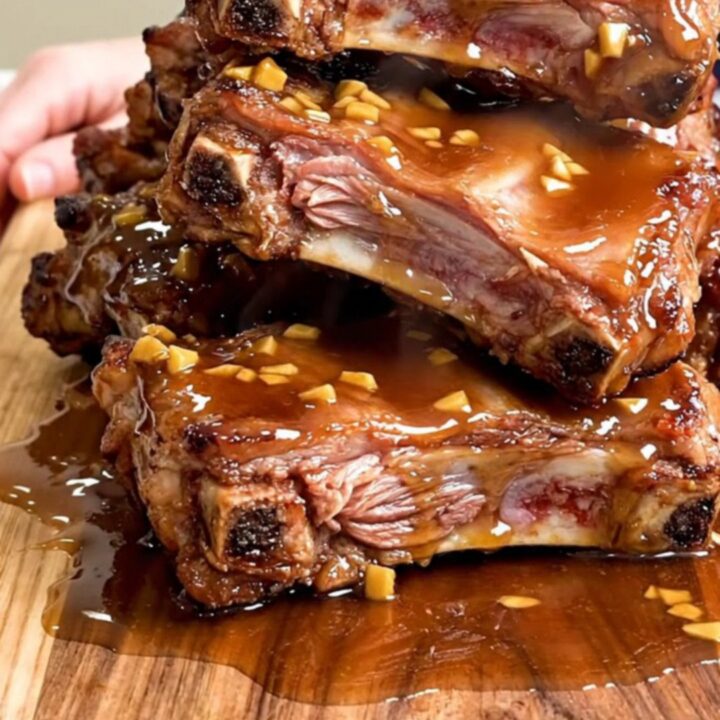 A close-up of tender, braised pork spareribs coated in a dark, glossy honey garlic sauce on a wooden board.