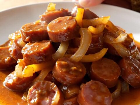 A stainless steel slow cooker filled with sliced kielbasa, colorful bell peppers, and onions in a rich, smoky paprika sauce.