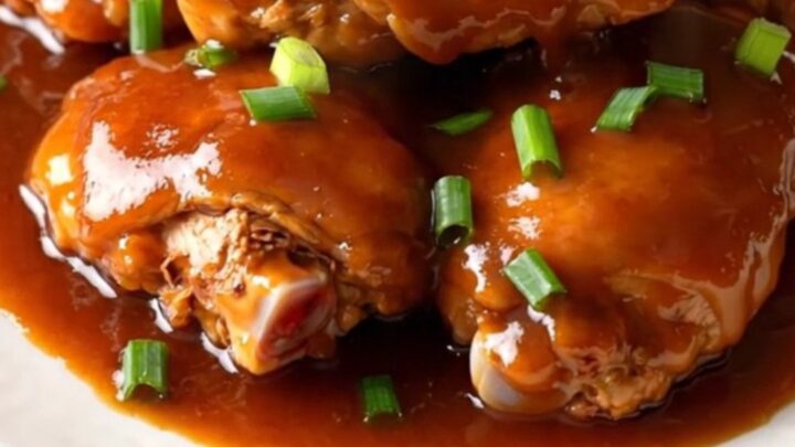 A top-down view of cooked chicken thighs in a slow cooker coated in a glossy red-brown sauce with green onions.