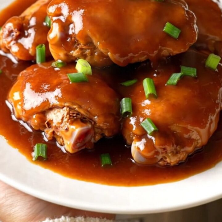 A top-down view of cooked chicken thighs in a slow cooker coated in a glossy red-brown sauce with green onions.