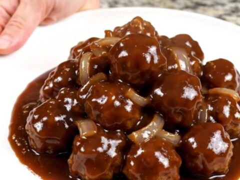 A close-up view of beef meatballs in a dark, glossy barbecue sauce inside a slow cooker.
