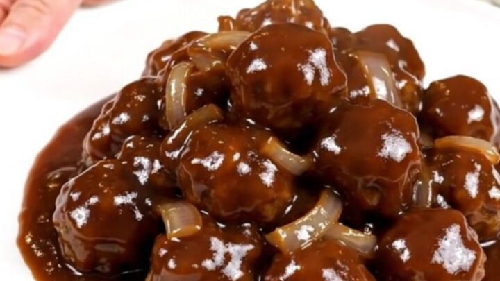 A close-up view of beef meatballs in a dark, glossy barbecue sauce inside a slow cooker.