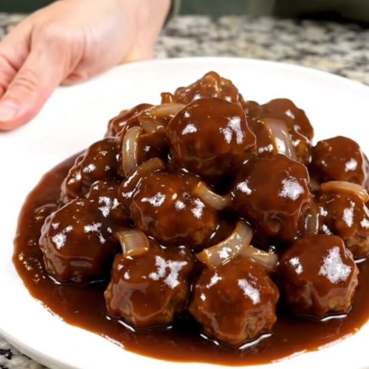 A close-up view of beef meatballs in a dark, glossy barbecue sauce inside a slow cooker.