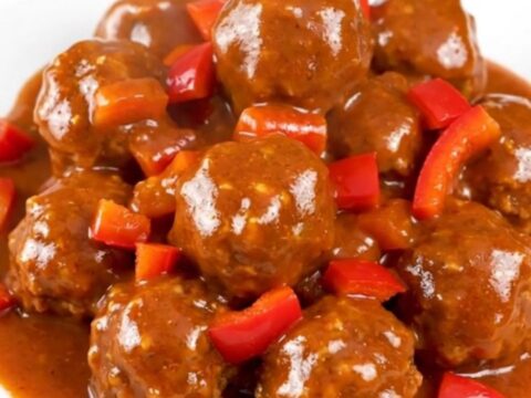 A top-down view of firecracker turkey meatballs in a black slow cooker, glazed in a vibrant red sauce.