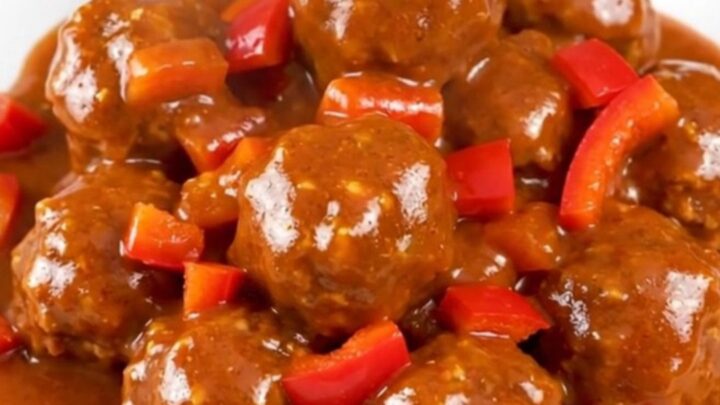 A top-down view of firecracker turkey meatballs in a black slow cooker, glazed in a vibrant red sauce.