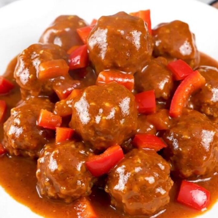 A top-down view of firecracker turkey meatballs in a black slow cooker, glazed in a vibrant red sauce.