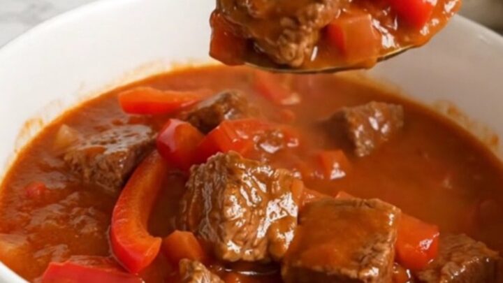 A steaming bowl of Hungarian beef goulash featuring tender braised beef cubes and red peppers in rich paprika sauce.