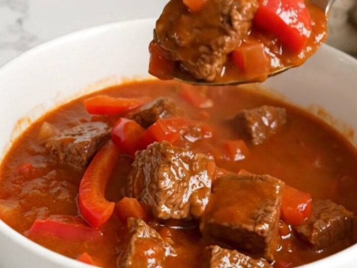 A steaming bowl of Hungarian beef goulash featuring tender braised beef cubes and red peppers in rich paprika sauce.