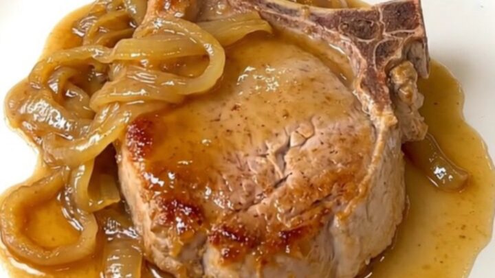 A plate of tender slow-cooked pork chops covered in a rich onion and soda sauce.