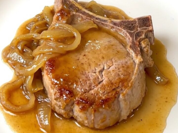 A plate of tender slow-cooked pork chops covered in a rich onion and soda sauce.