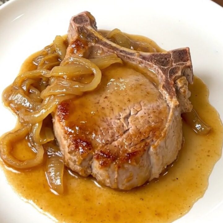 A plate of tender slow-cooked pork chops covered in a rich onion and soda sauce.