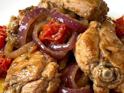 A top-down view of cooked chicken gyro meat with onions and tomatoes in a black slow cooker.