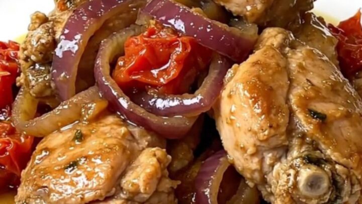 A top-down view of cooked chicken gyro meat with onions and tomatoes in a black slow cooker.