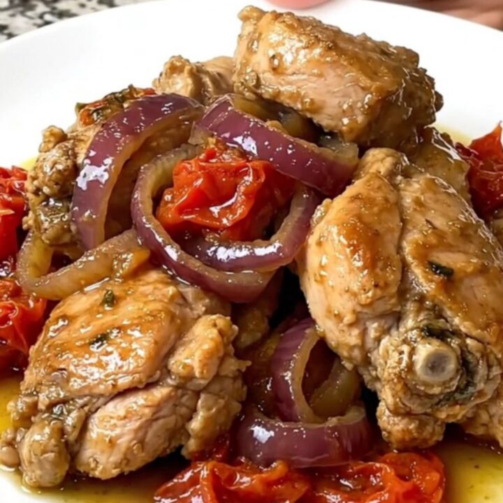 A top-down view of cooked chicken gyro meat with onions and tomatoes in a black slow cooker.