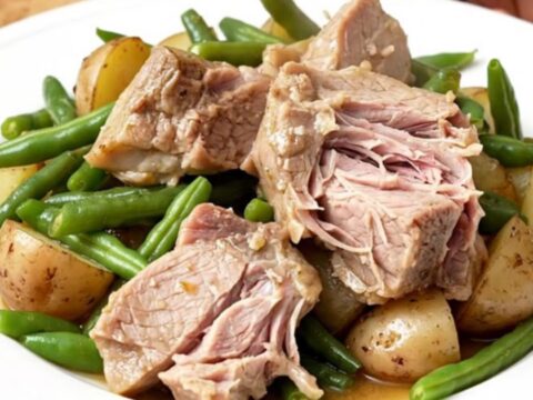 A rustic slow cooker filled with tender pork shoulder chunks, baby potatoes, and fresh green beans.
