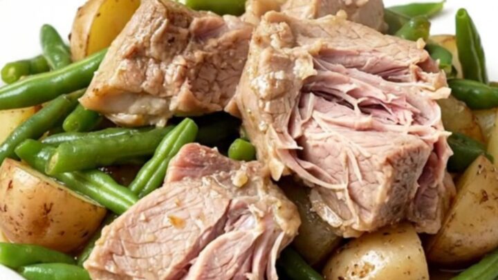 A rustic slow cooker filled with tender pork shoulder chunks, baby potatoes, and fresh green beans.