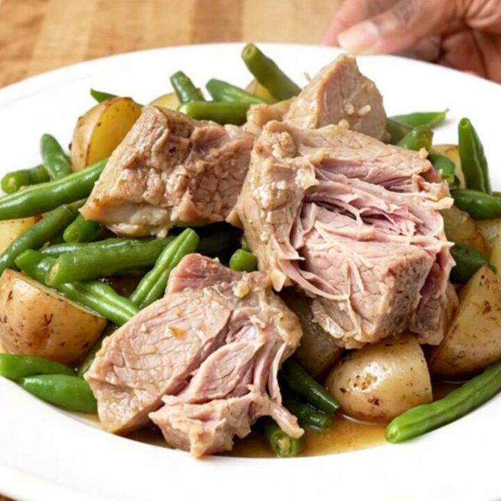A rustic slow cooker filled with tender pork shoulder chunks, baby potatoes, and fresh green beans.