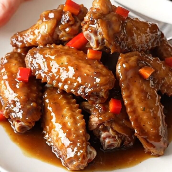 A close-up of tender, slow-cooked jerk turkey wings with peppers and scallions in a black slow cooker.