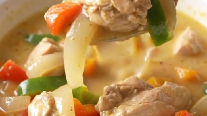 A bowl of creamy Philly chicken cheesesteak soup with visible chicken strips, peppers, and onions.