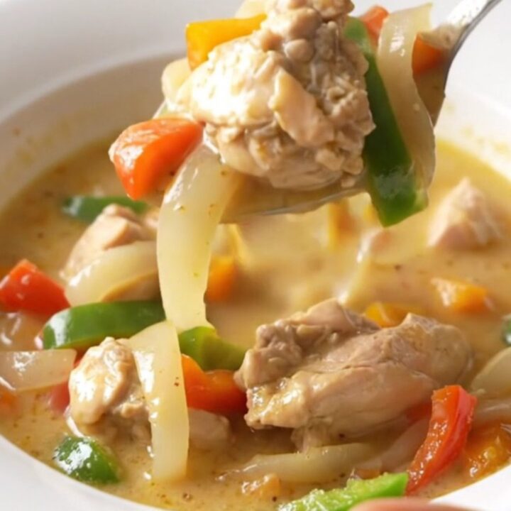 A bowl of creamy Philly chicken cheesesteak soup with visible chicken strips, peppers, and onions.