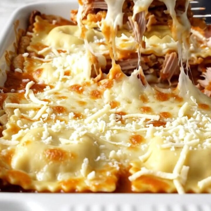 A top-down view of a rectangular baking dish filled with layers of ravioli, turkey, and melted mozzarella cheese.