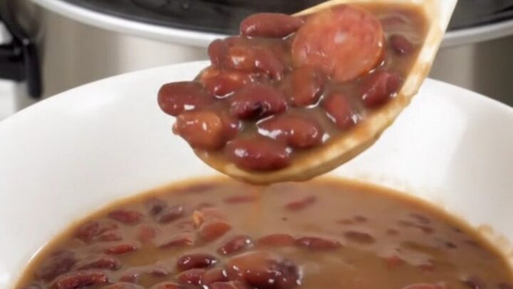 A top-down view of a black slow cooker filled with red beans and sliced smoked sausage.