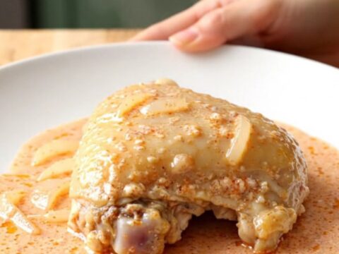 A close-up of tender chicken thighs covered in a rich, creamy pink vodka sauce on a white plate.