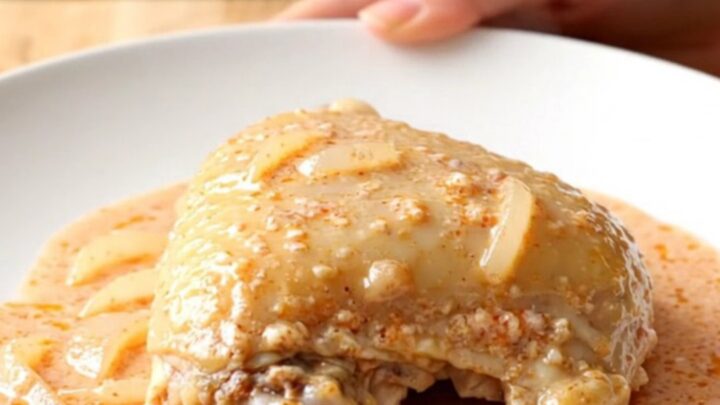 A close-up of tender chicken thighs covered in a rich, creamy pink vodka sauce on a white plate.
