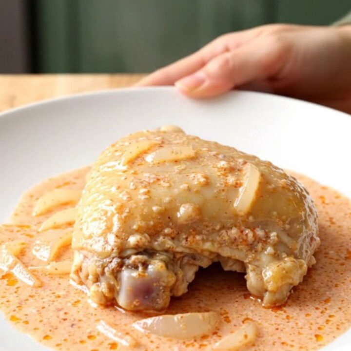 A close-up of tender chicken thighs covered in a rich, creamy pink vodka sauce on a white plate.