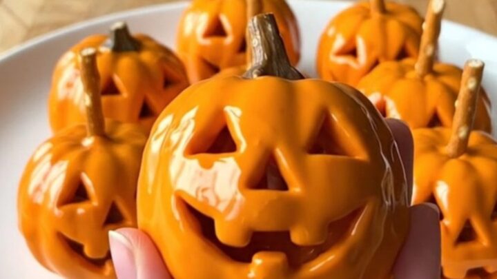 A dozen bright orange Jack-O'-Lantern crispy rice treat balls arranged in rows on a parchment-lined baking sheet.
