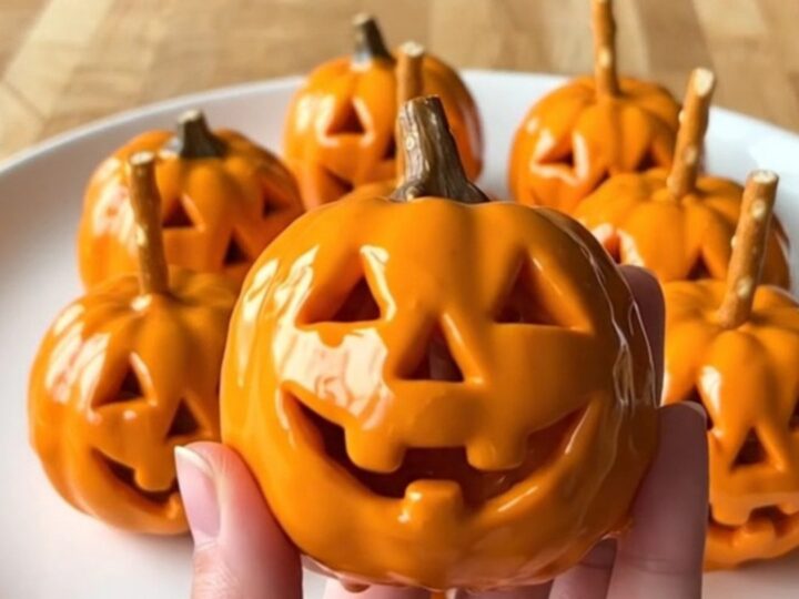 A dozen bright orange Jack-O'-Lantern crispy rice treat balls arranged in rows on a parchment-lined baking sheet.