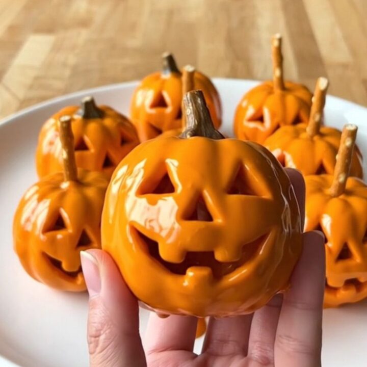 A dozen bright orange Jack-O'-Lantern crispy rice treat balls arranged in rows on a parchment-lined baking sheet.