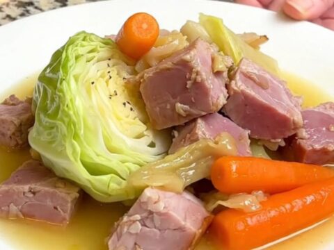 A warm, rustic bowl of slow-cooked ham, tender cabbage wedges, and bright orange carrots in a savory broth.